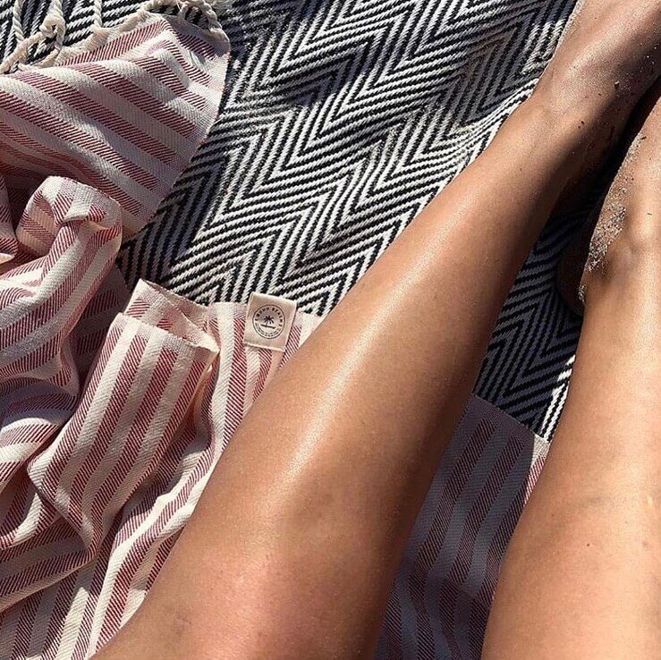 Solbrune ben ovenpå et farverigt strandhåndklæde og smukt strandtæppe